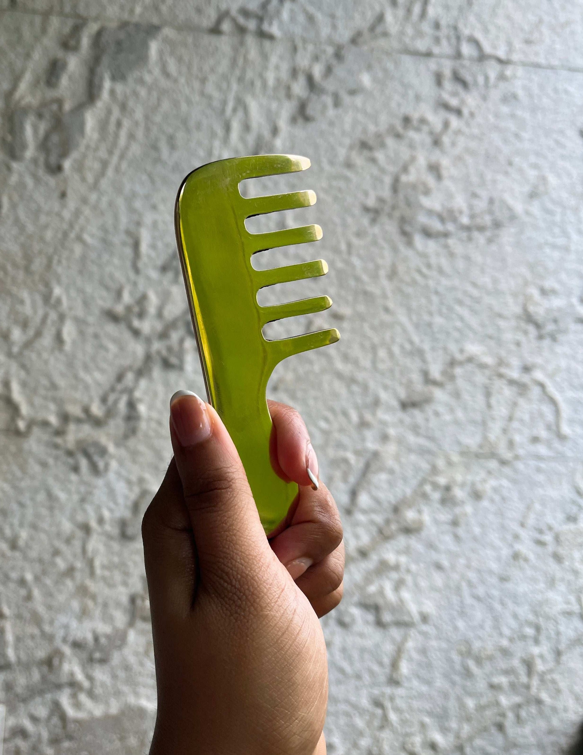 Hand holding a green Kansa hair kanga comb for traditional kansa hair massage and scalp care – crafted from kansa metal for natural wellness